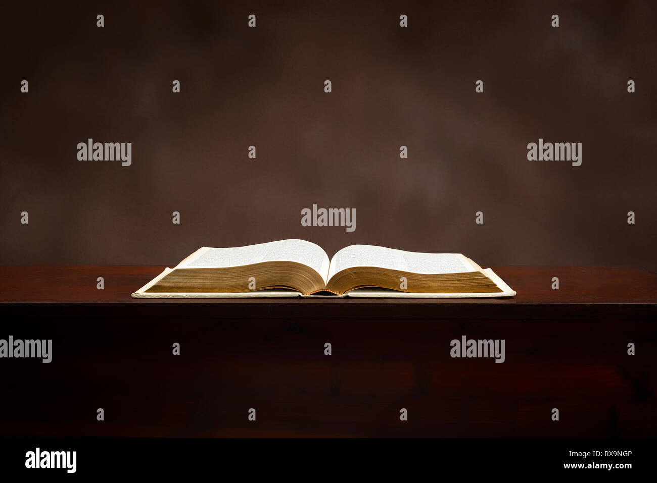 Inquadratura orizzontale di una vecchia Bibbia giacente aperta su uno sfondo di colore marrone. Foto Stock