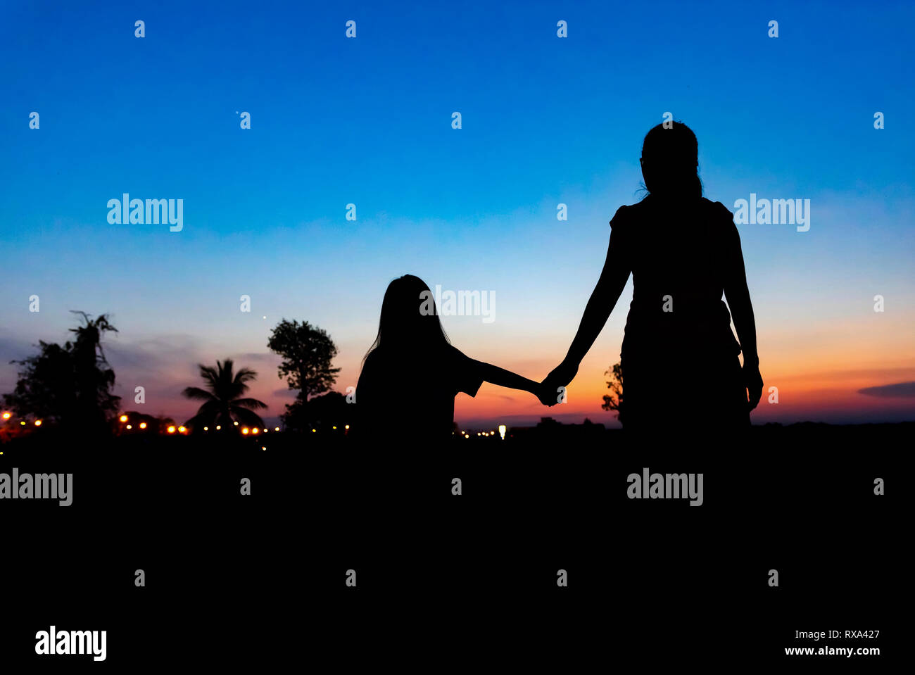 Vista posteriore della silhouette a madre e figlia per mano mentre in piedi contro il cielo drammatico durante il tramonto Foto Stock