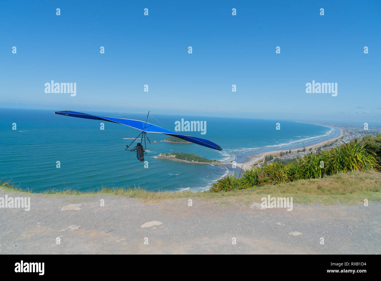 Il decollo pilota hanglider salta fuori pista con pittoresche spiagge di Mount Maunganui allungamento all' orizzonte di seguito. Foto Stock