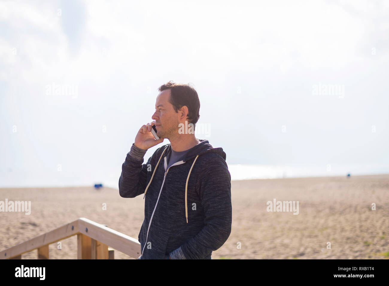 Uomo che ascolta al telefono intelligente mentre si sta in piedi in spiaggia contro sky Foto Stock