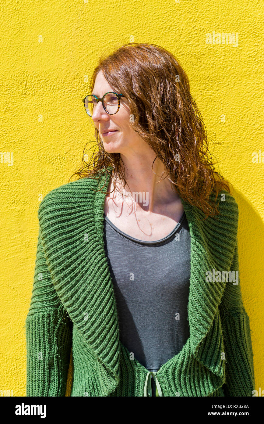 Fiducioso imprenditrice che guarda lontano mentre in piedi contro la parete gialla durante la giornata di sole Foto Stock