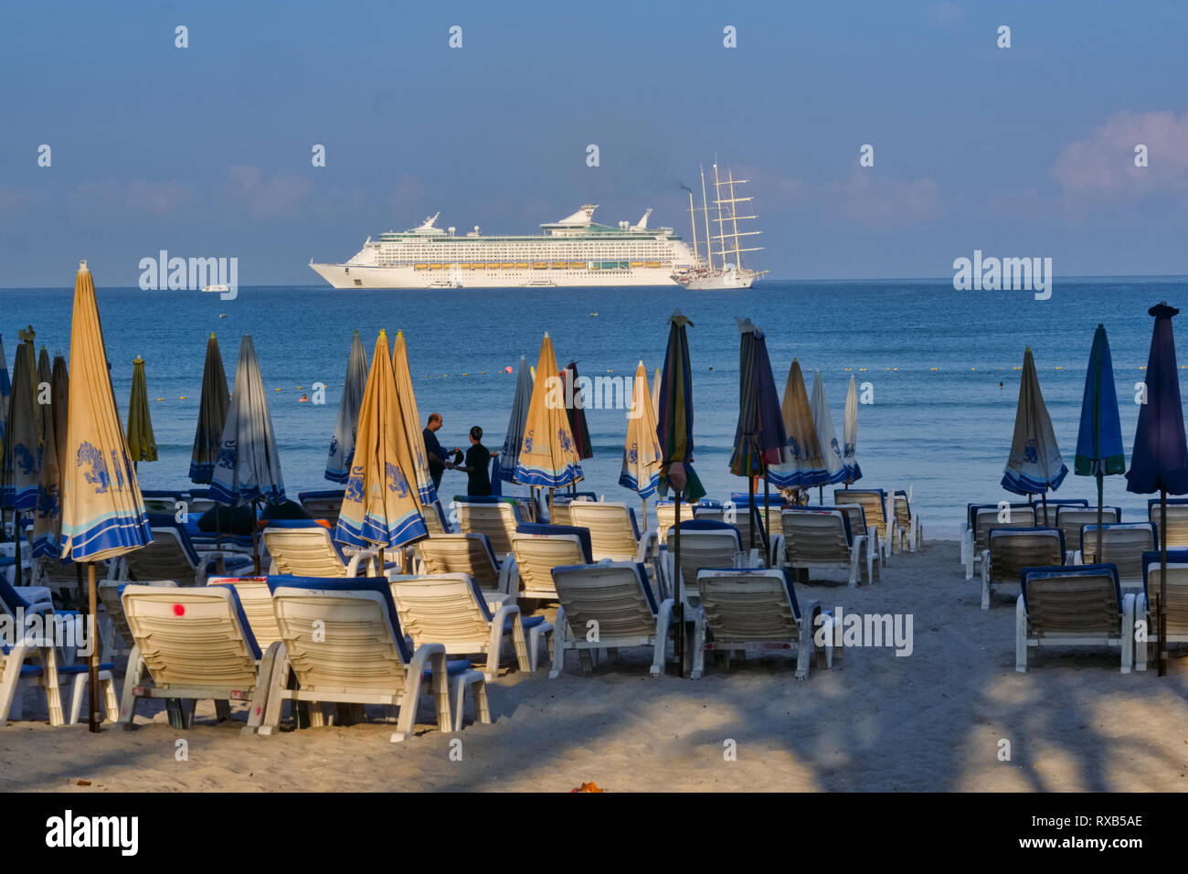 La mattina presto a Patong Beach, Phuket, Thailandia, con ombrelloni e sedie a sdraio in primo piano una grande nave da crociera achored off shore Foto Stock