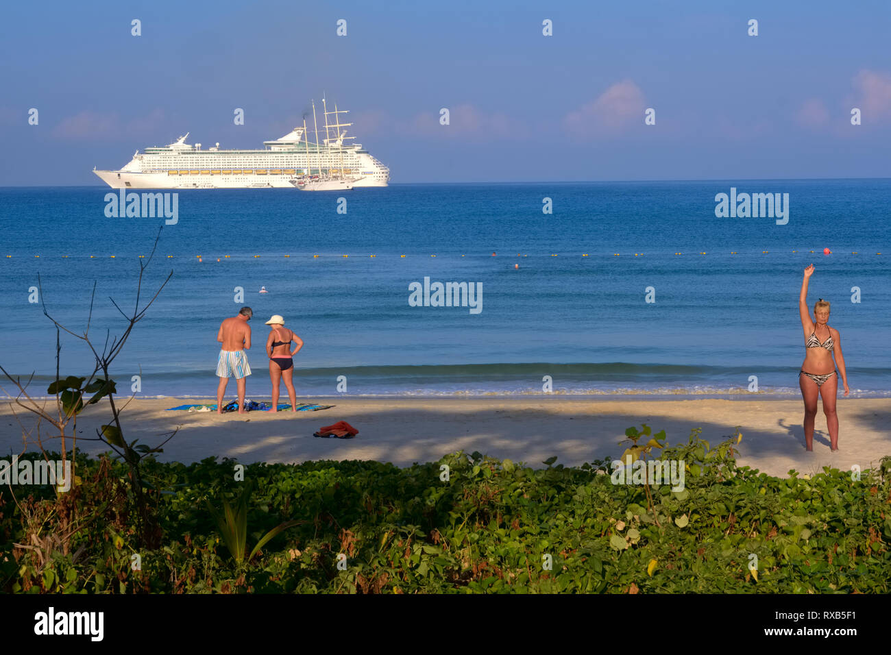 A Patong Beach, Phuket, Thailandia, una donna (r) sta facendo esercizi leggeri, con un turista giovane e una nave da crociera in background Foto Stock