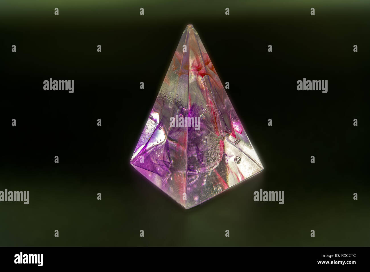 Peso della carta in vetro multicolore su sfondo scuro sfocato, che mostra vivaci tonalità di viola e rosso in un design a forma di piramide Foto Stock