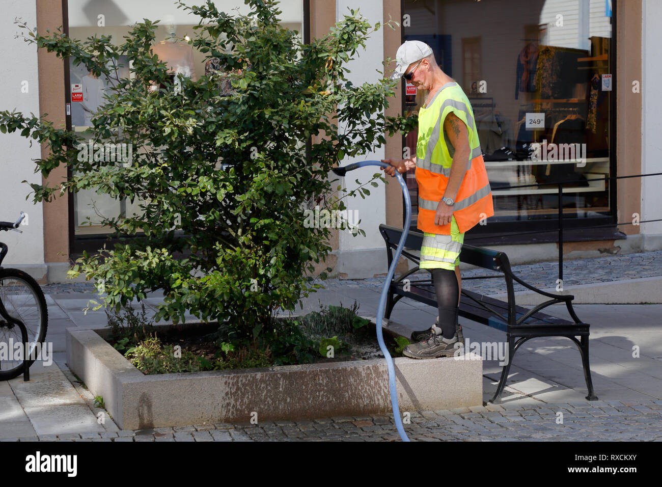 Karlskrona, Svezia - 23 agosto 2017: un uomo in abiti da lavoro impianto di irrigazione con tubo in ambiente urbano Foto Stock