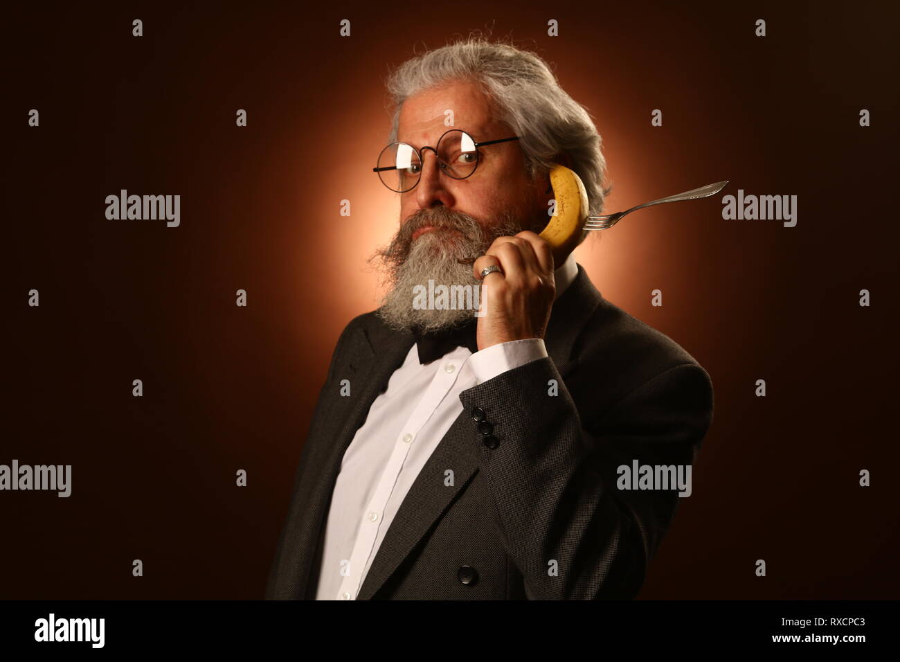 Ritratto di un grey-haired anziano gentiluomo con un shaggy i baffi e barba, in una camicia bianca e giacca grigia, indossare occhiali e una forcella, tenendo un Foto Stock