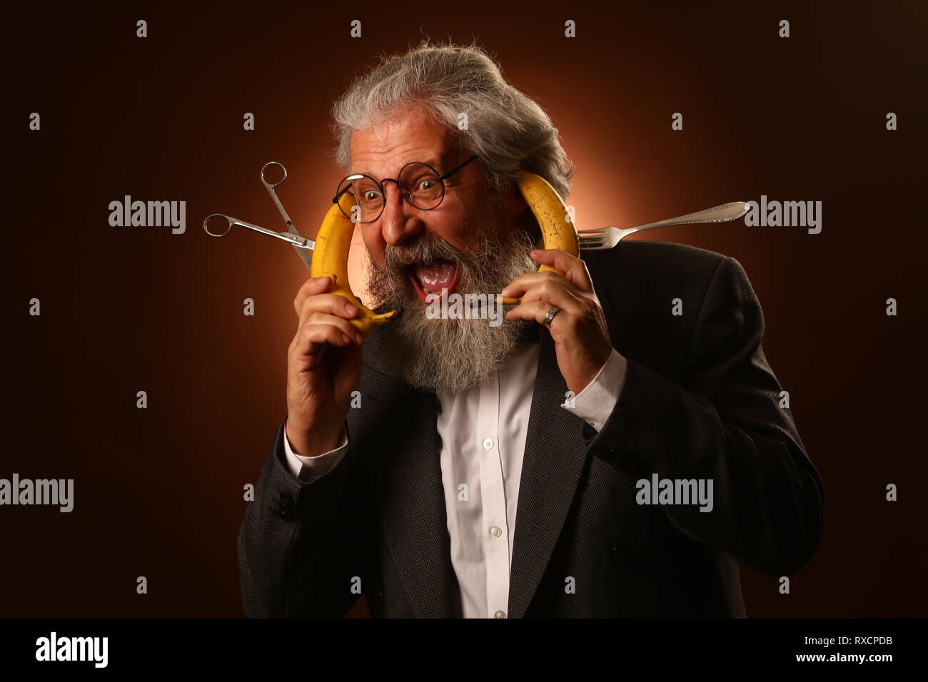 Ritratto di un grey-haired anziano gentiluomo con un shaggy i baffi e barba, in una camicia bianca e giacca grigia, indossare occhiali e una forcella, tenendo un Foto Stock