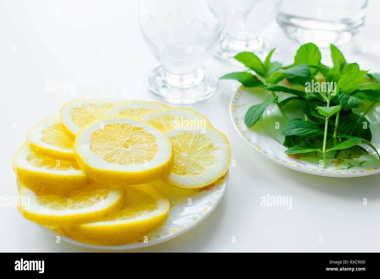 Estate istituito dalla preparazione della bevanda rinfrescante con foglie di menta fresca e succose fette di limone con due bicchieri in background. Foto Stock