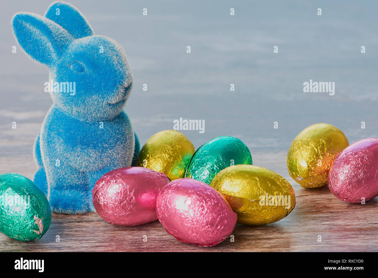 Blu coniglietto di pasqua con avvolto di uova di cioccolato contro il bianco sullo sfondo di legno con spazio di copia Foto Stock