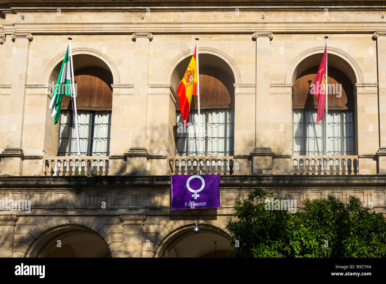 Quattro bandiere montati nella parte anteriore del Siviglia city hall. Il piccolo purple​ uno è per il 8 marzo 2019, giorno della donna Foto Stock