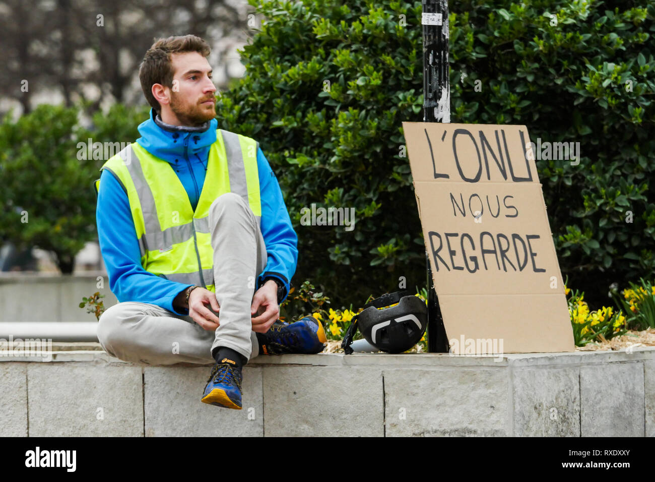Lione, Francia, 9 Marzo 2019: un manifestante è visto seduto vicino a un pannello a leggere 'ONU (Nazioni Unite) ci guarda come si vede nella Lione centro-orientale (Francia) in occasione della XVII Giornata di azione organizzata dalle giacche gialle per protestare Emmanuel Macron la politica del governo. Credito Credito: Serge Mouraret/Alamy Live News Foto Stock