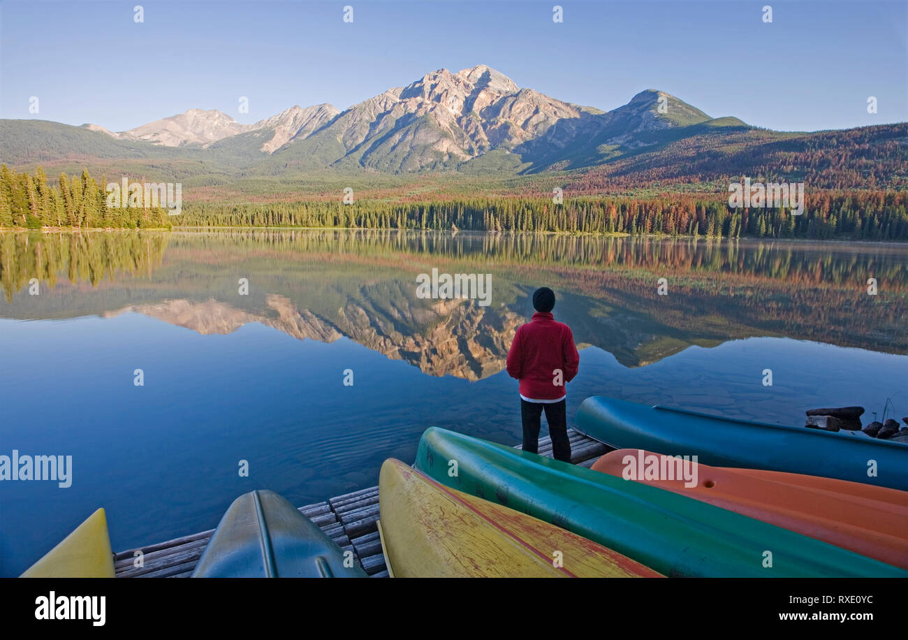 Lone medio di sesso maschile di età in piedi sul dock con canoe guardando a piramide in Montagna Lago Piramide, il Parco Nazionale di Jasper, Alberta, Canada Foto Stock