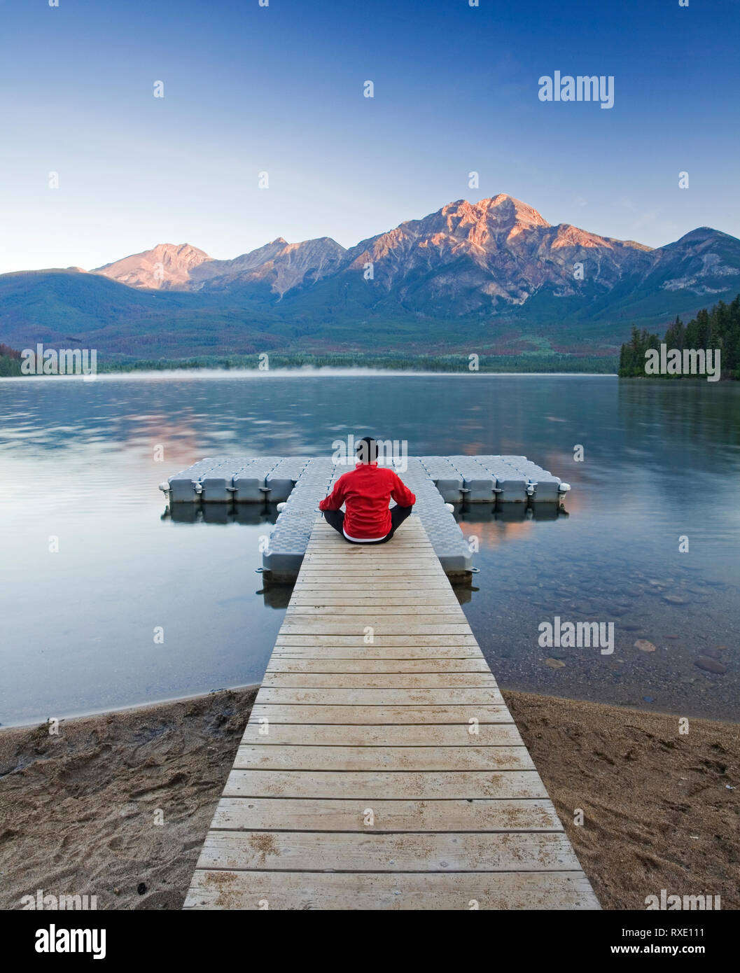 Uomo seduto sul dock meditando a Lago Piramide, il Parco Nazionale di Jasper, Alberta, Canada. Foto Stock