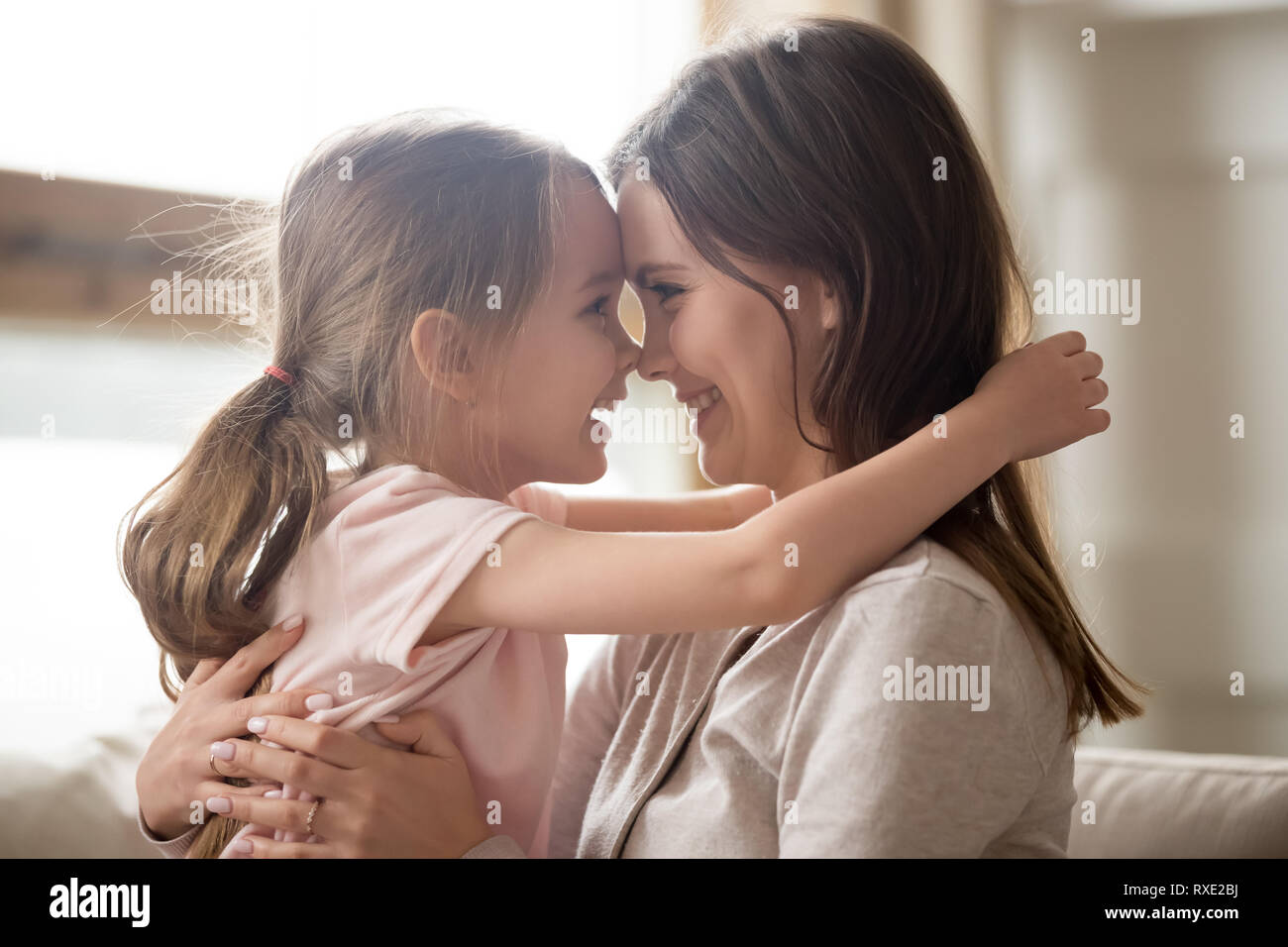 Carino kid ragazza sorridente che abbraccia la mamma toccando nasi avente fun Foto Stock