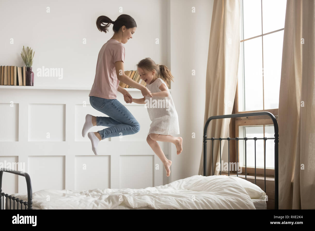 Felice mamma e bambino ragazza tenendo le mani di saltare sul letto Foto Stock