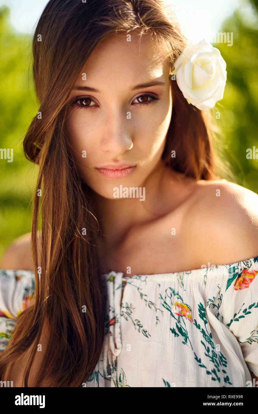 Un ritratto di una donna con rosa bianca tra i capelli con la luce del sole splende in giù su di lei. Foto Stock