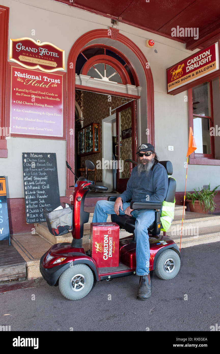 Uomo su uno scooter di mobilità con una cassa di birra Foto Stock