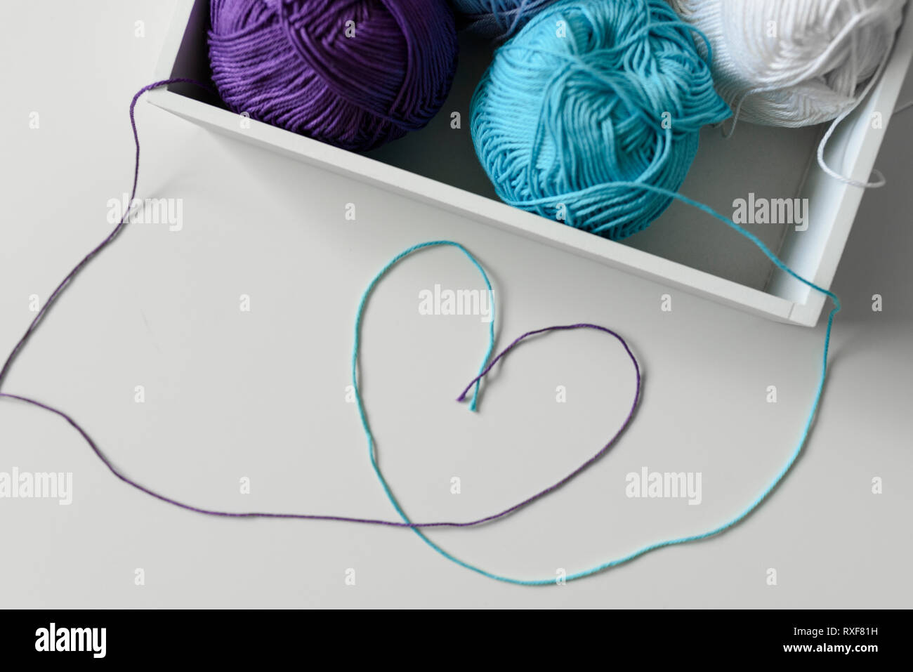 Il simbolo del cuore di progettato da i fili colorati al di fuori della casella bianca con filati per maglieria a sfere. Foto Stock
