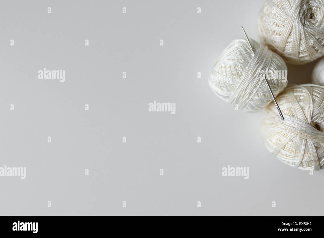 Ago e filo per cucire su sfondo bianco con copia spazio. Vista superiore del beige filato di cotone palle. Foto Stock