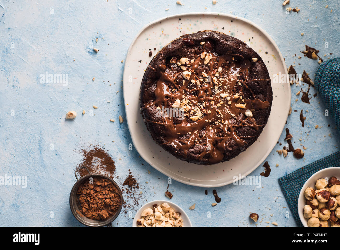 Torta al cioccolato con nocciole tritate su un bianco di forma irregolare piastra su un blu sfondo testurizzata Foto Stock