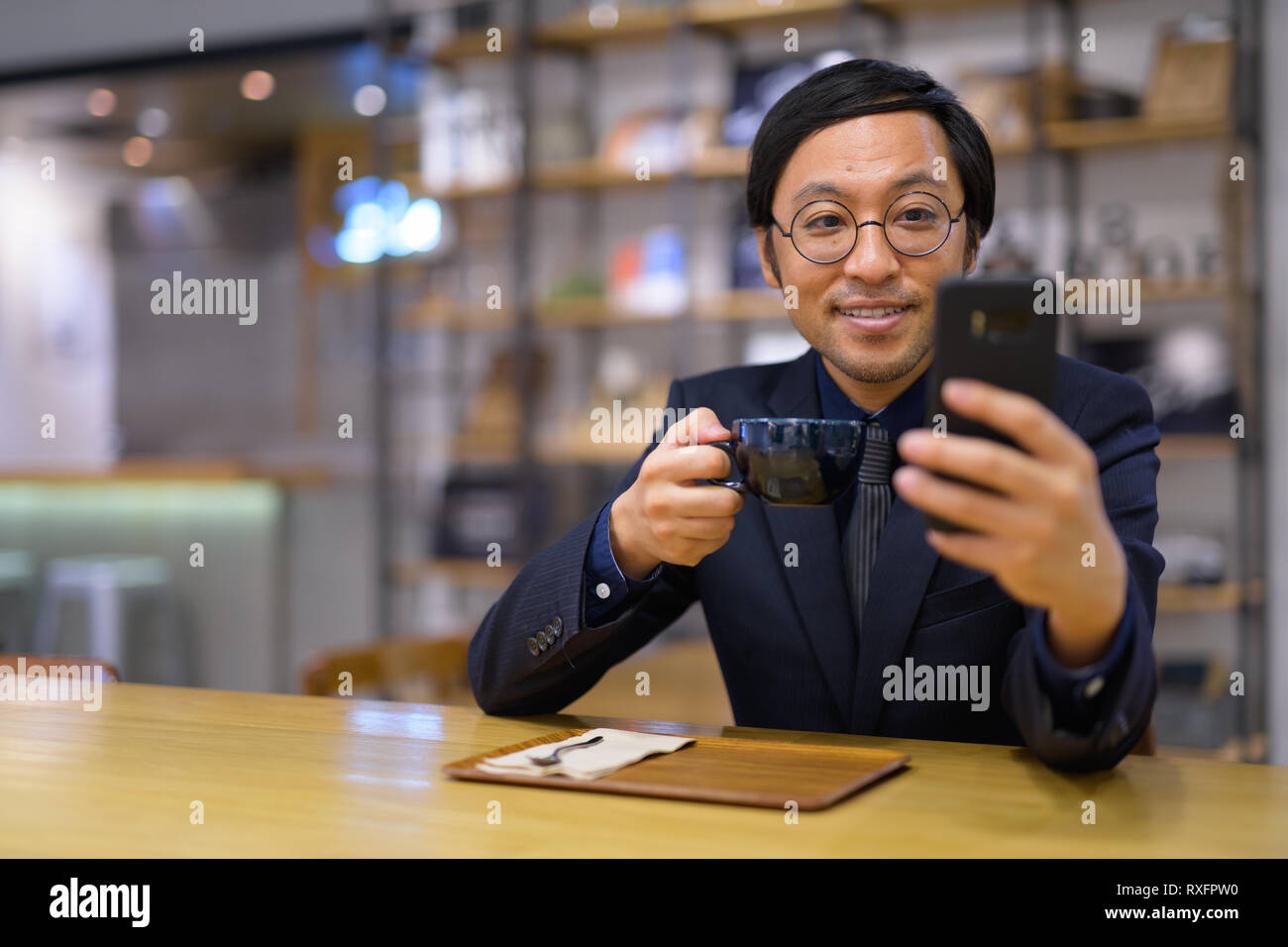 Happy businessman asiatici utilizzando il telefono mentre si beve caffè Foto Stock