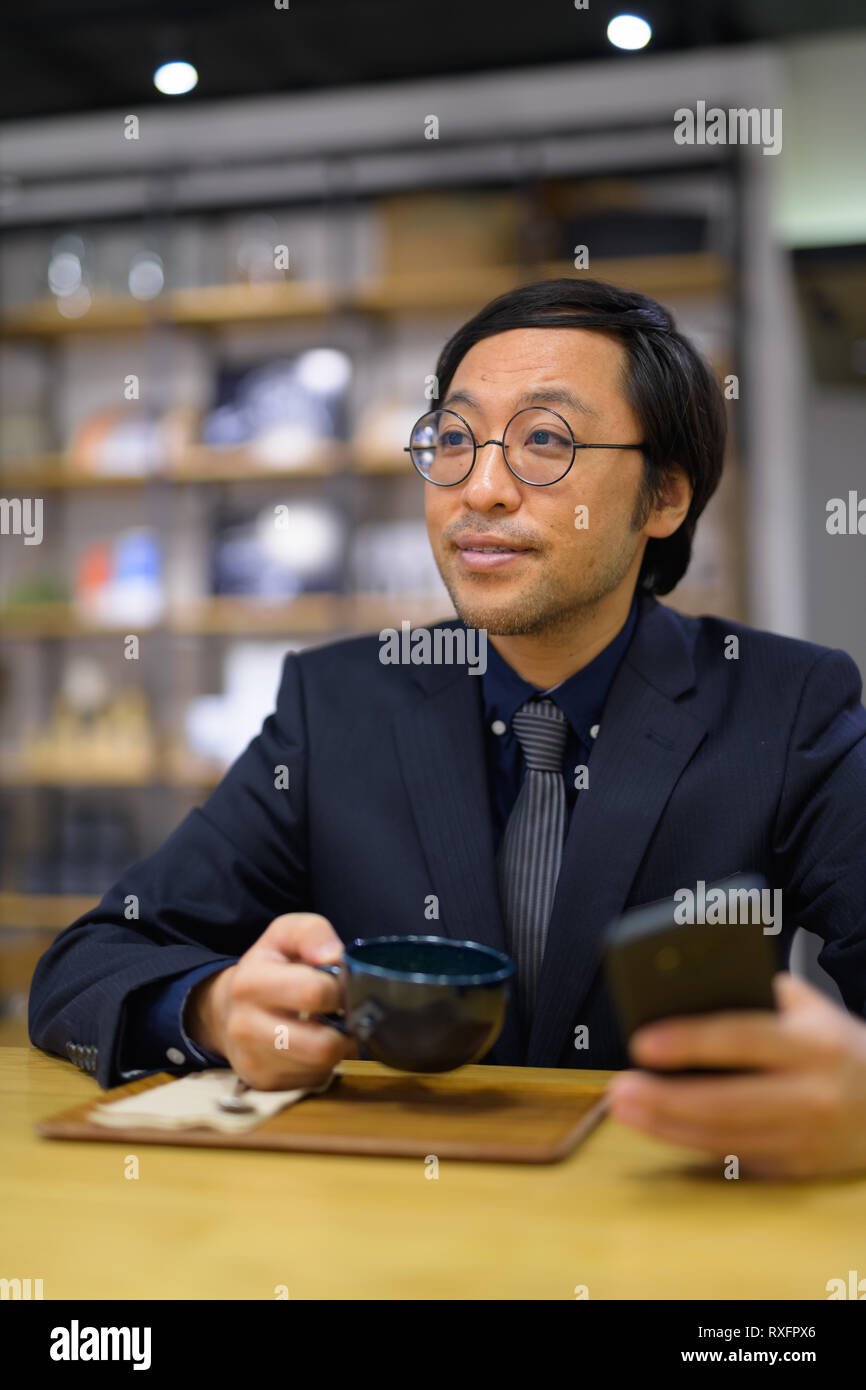 Happy businessman asiatici pensando tenendo tazza da caffè e telefono Foto Stock
