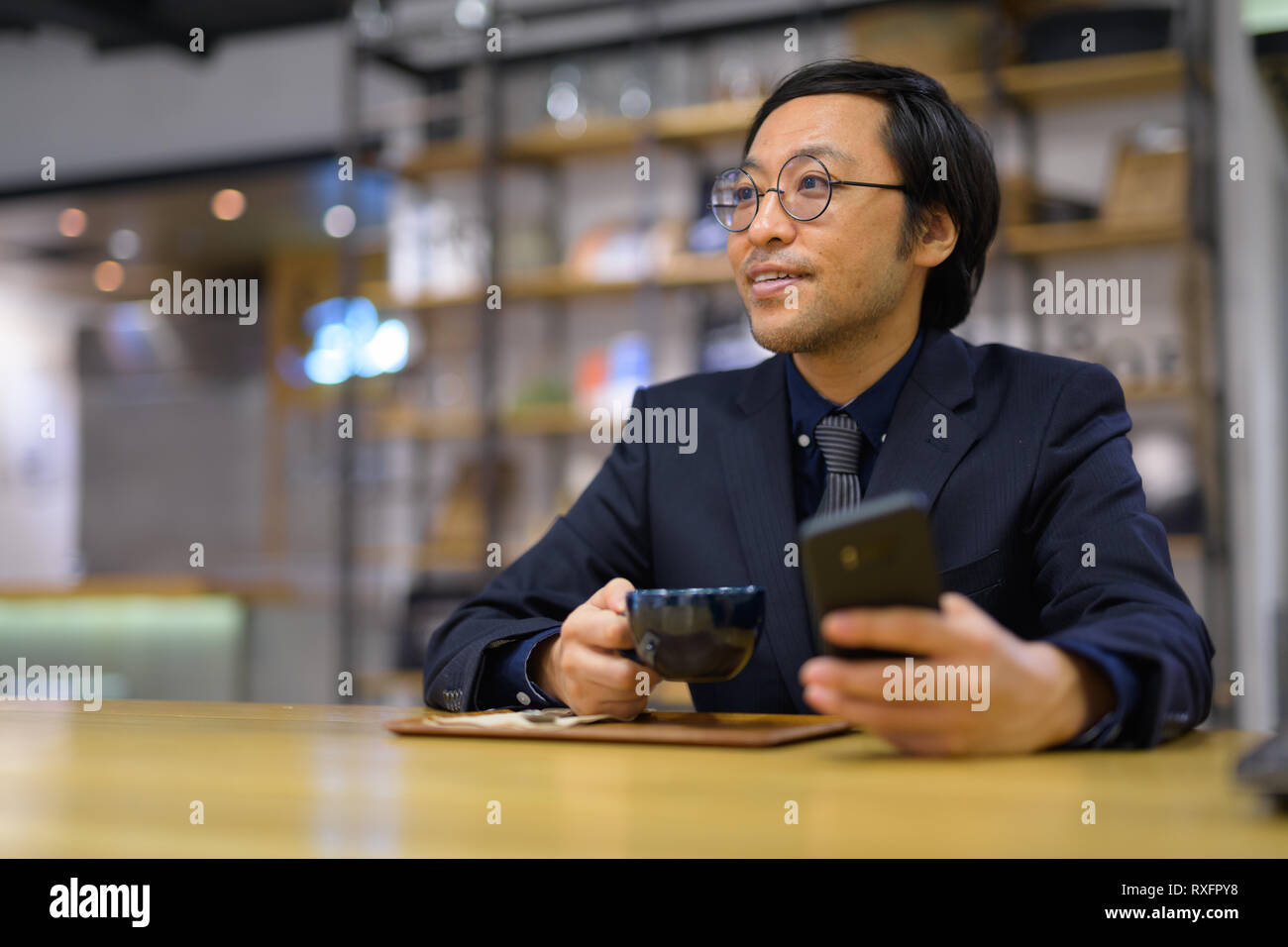 Happy businessman asiatici pensando tenendo tazza da caffè e telefono Foto Stock