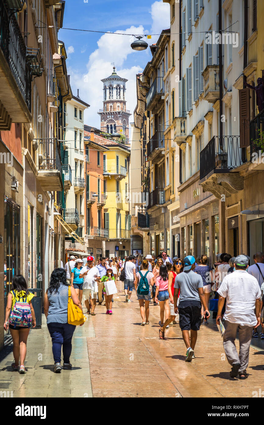 Immagine da Via Giuseppe Mazzini con molti negozi e turisti con la Torre dei Lamberti in background in una giornata di sole Foto Stock