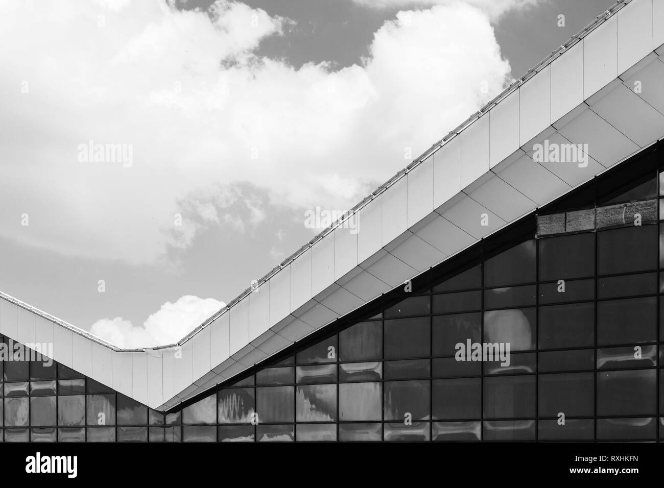 In bianco e nero una moderna facciata in vetro e contro lo sfondo blu cielo nuvoloso Foto Stock