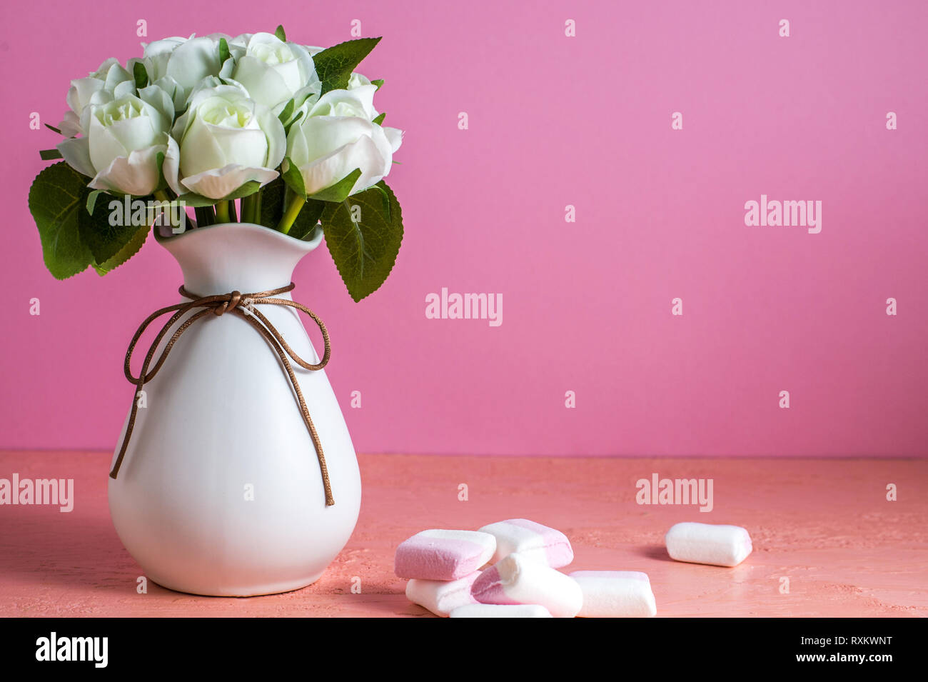 Copyspace con colorati mini marshmallows su un tavolo accanto a rose bianche su sfondo rosa Foto Stock