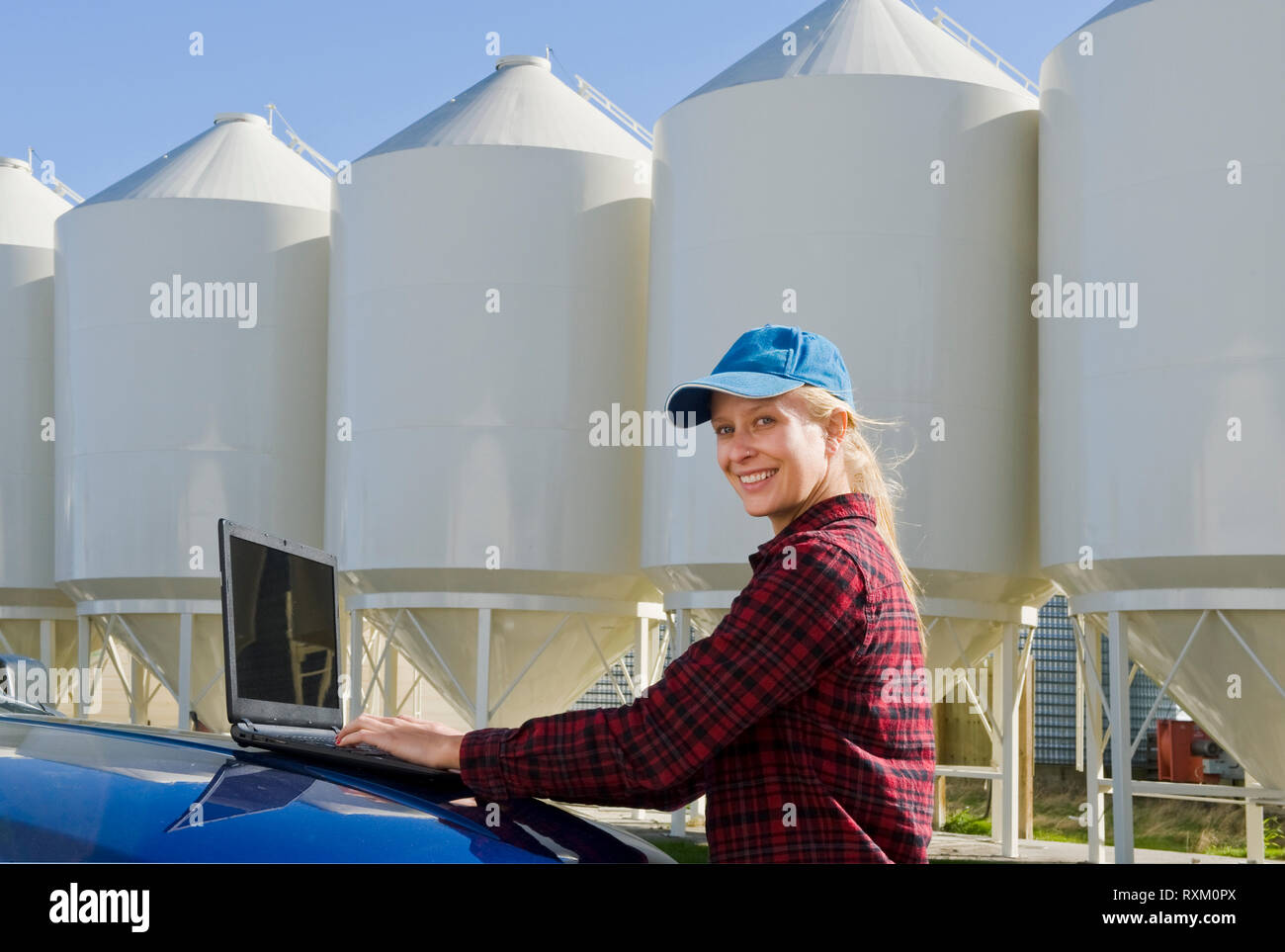 Ragazza utilizzando un computer accanto al deposito di seme contenitori tramoggia nel cortile di una fattoria, nei pressi di Dugald, Manitoba Foto Stock