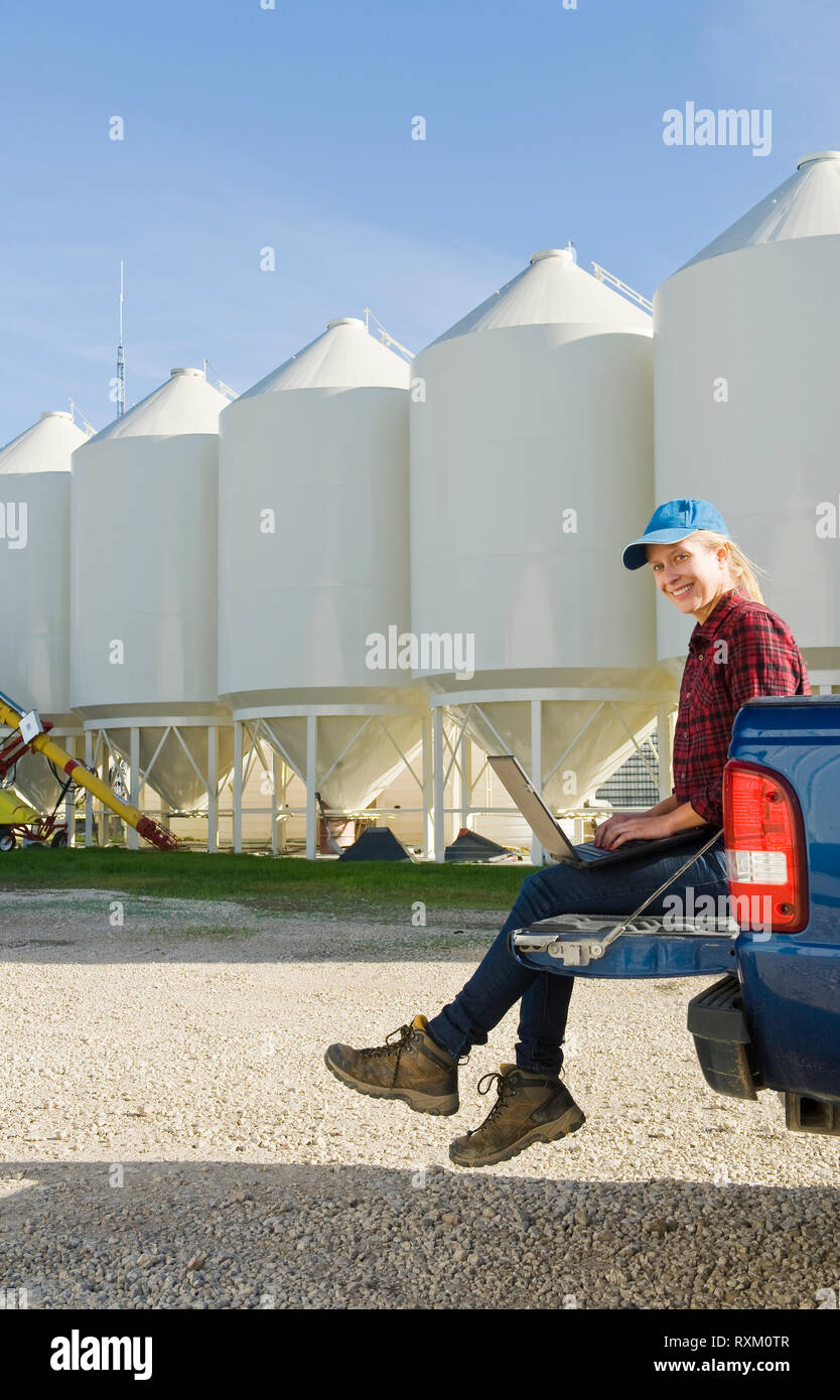 Ragazza utilizzando un computer accanto al deposito di seme contenitori tramoggia nel cortile di una fattoria, nei pressi di Dugald, Manitoba Foto Stock