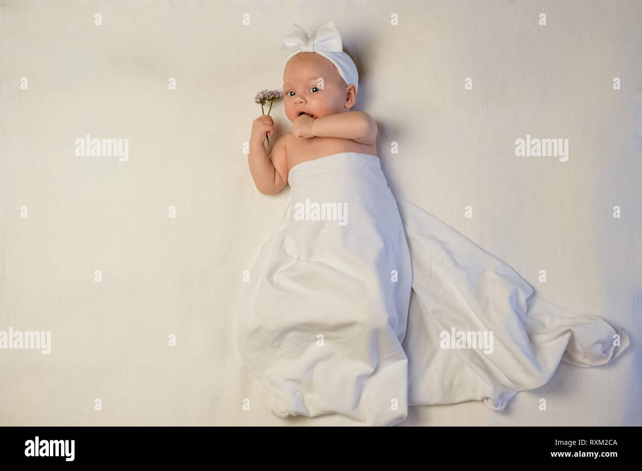 Bellissima bambina tenendo un fiore su coltre bianca Foto Stock