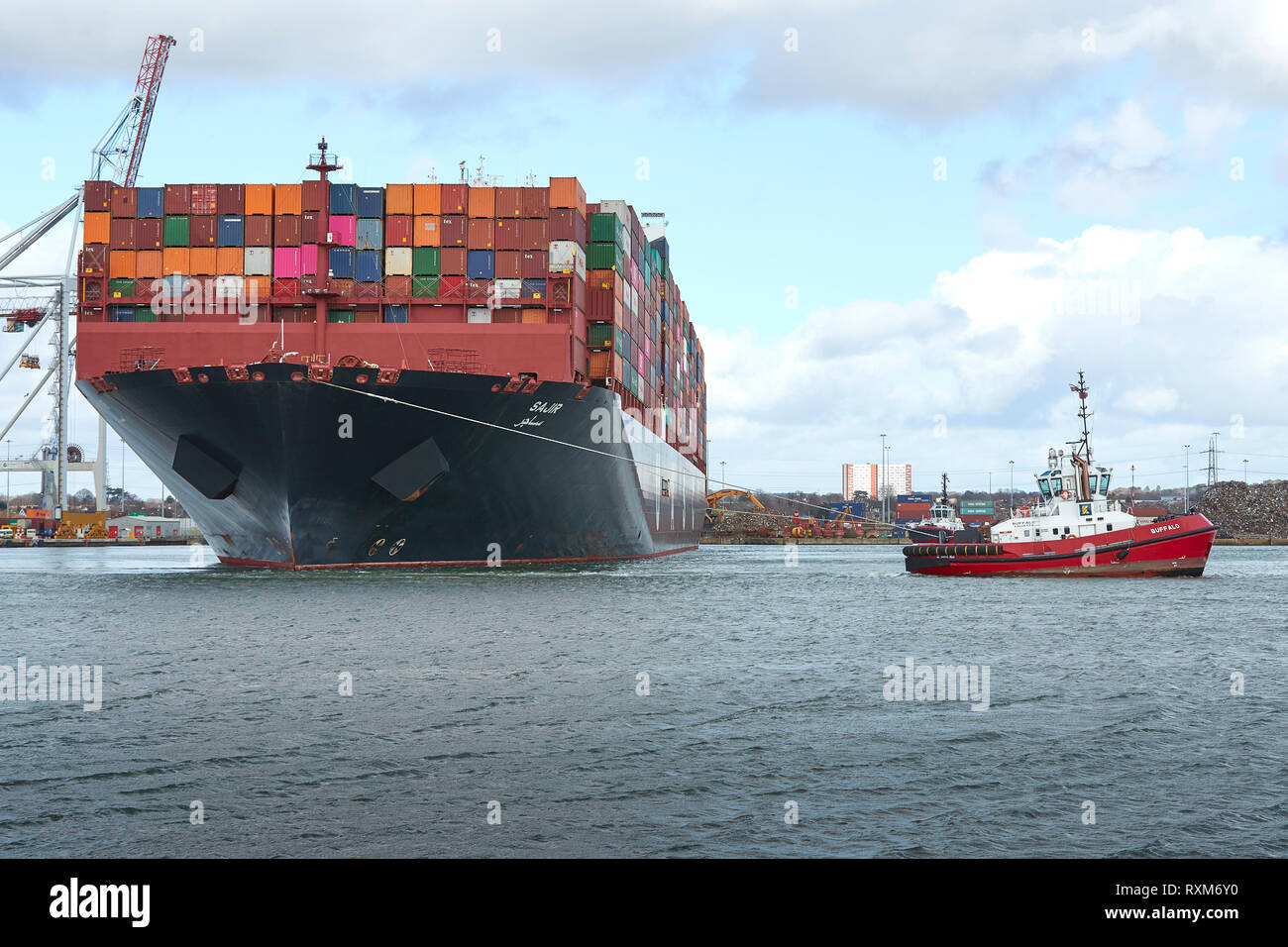 Tre rimorchiatori assistono la nave portacontainer ultra-large SAJIR, in partenza dal Southampton Container Terminal, Hampshire, Regno Unito. Foto Stock