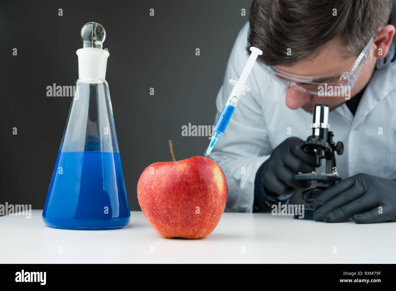 Ai giovani scienziati utilizzando blu liquido, Apple, siringa e microscopio su un bianco tavolo di laboratorio. Alimenti geneticamente modificati ricerca concetto astratto. Foto Stock