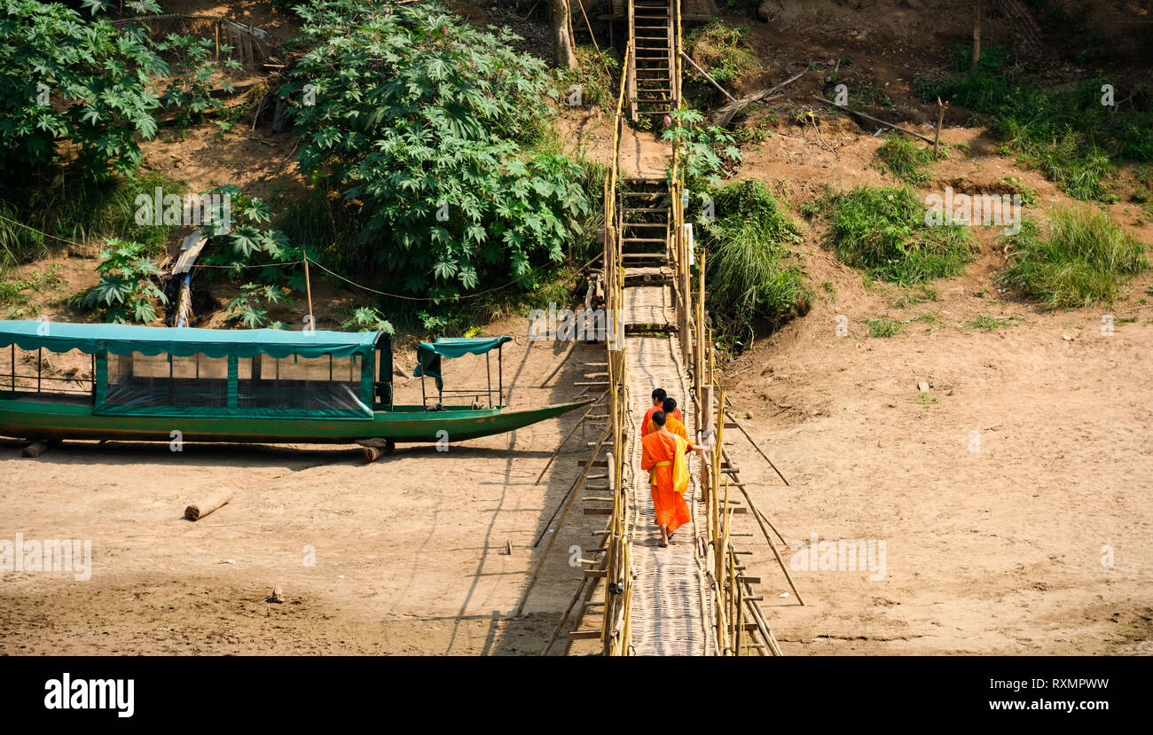 Non identificato tre monaci buddisti stanno attraversando il ponte di bambù che attraversano il fiume Nam Khan. Foto Stock