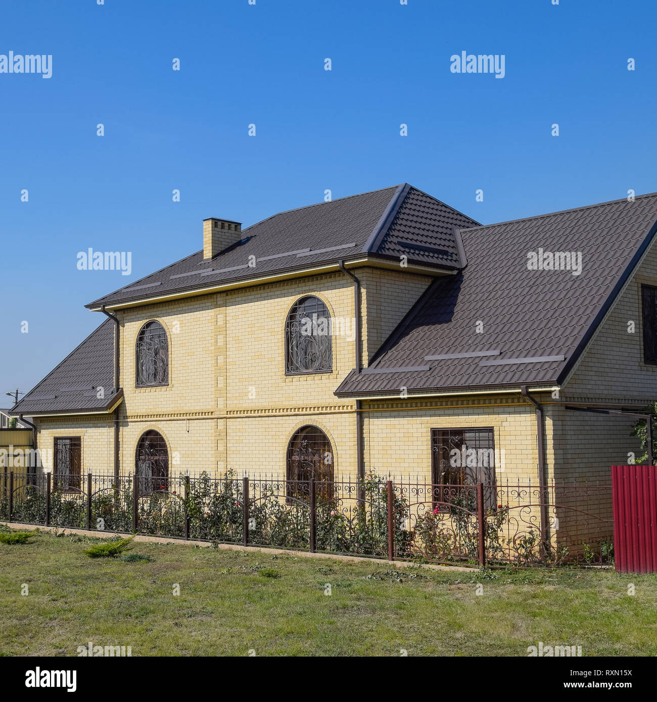 Casa del mattone giallo e marrone e tetto ondulato in metallo. Tralicci su windows Foto Stock