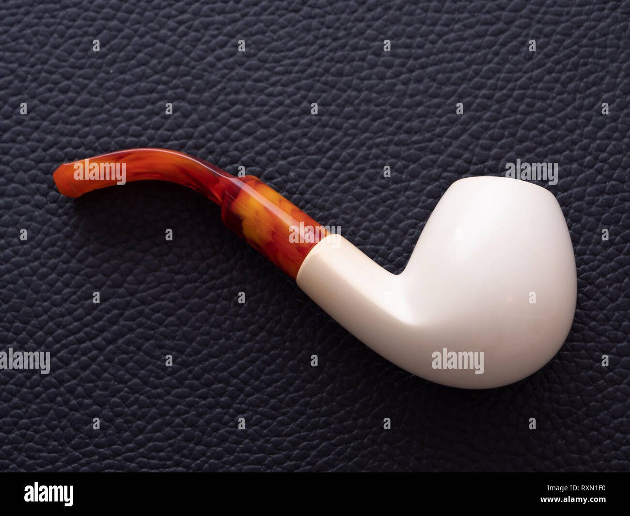 Un elegante e semplice bianco Meerschaum tubo con un boccaglio Giallo su nero lo sfondo in pelle Foto Stock