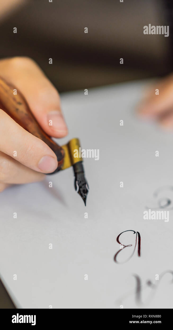 Calligrapher mani scrive una frase sul libro bianco. Inscrivendo ornamentali in lettere decorate. La calligrafia, graphic design, scritte, la grafia Foto Stock