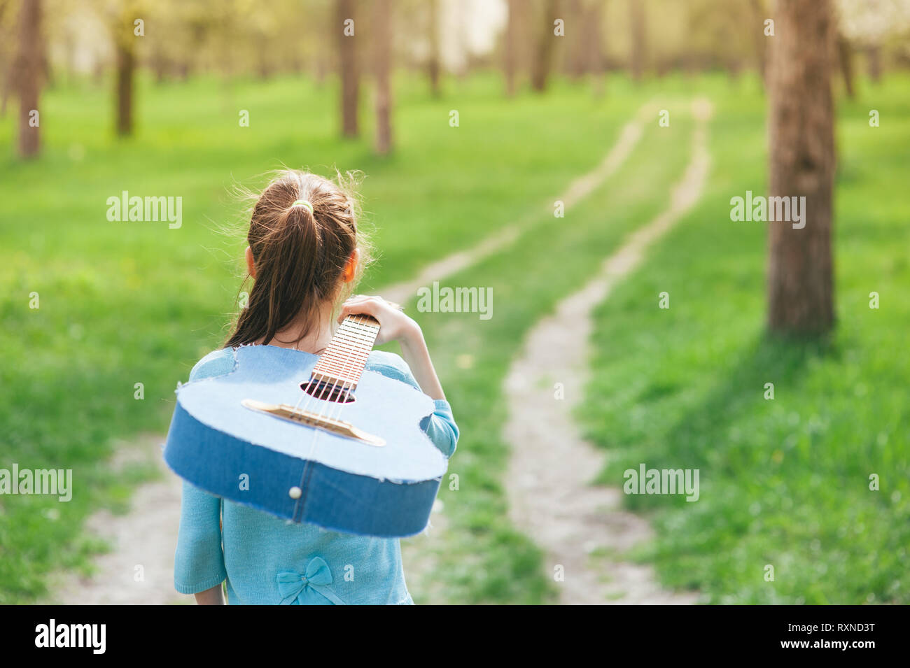 Concetto di vagrant giovane musicista piccola ragazza camminare outdoor primavera park lungo il sentiero che porta acustico denim spagnolo chitarra sulla sua spalla Foto Stock