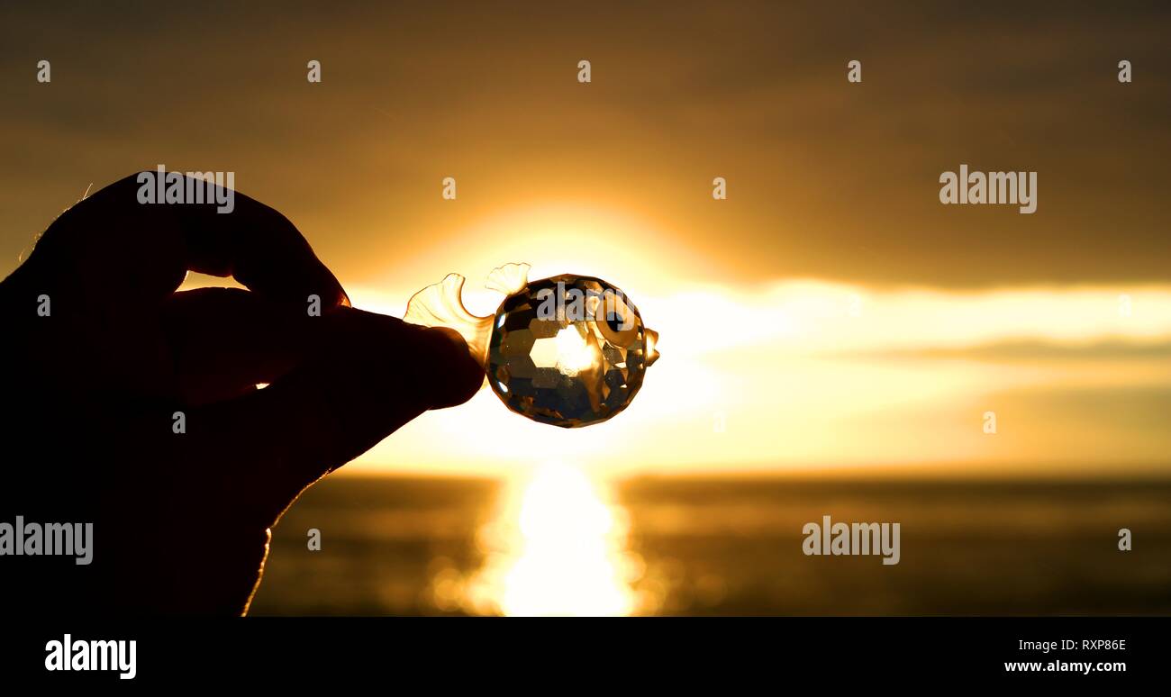 Tenendo in mano un cristallo contro il tramonto Foto Stock