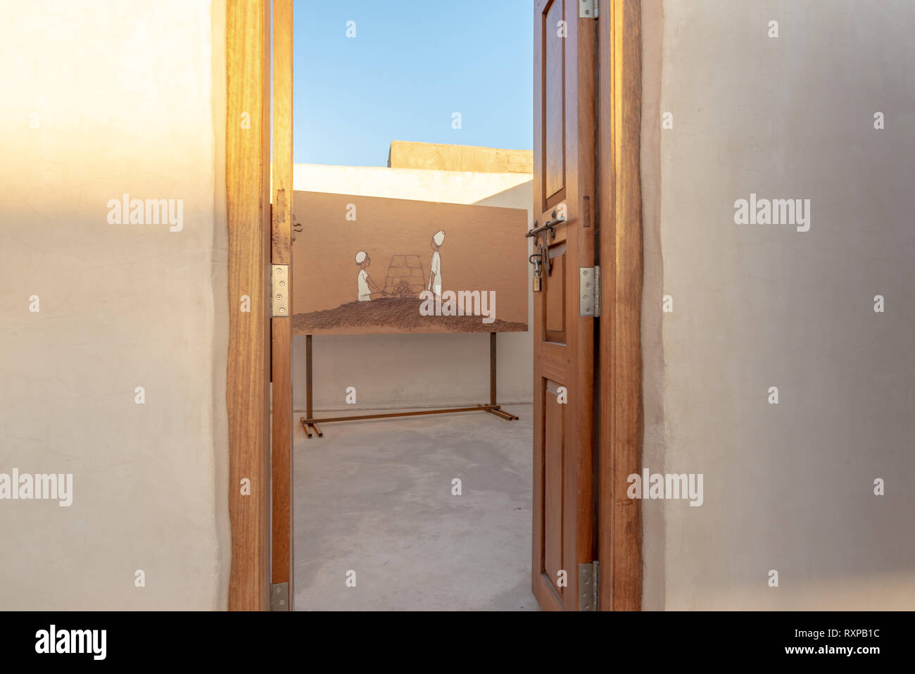 Apertura della porta su un dipinto come parte di una mostra d'arte nel villaggio abandonned di Al Jazirah Al Hamra al tramonto, emirato di Ras Al Khaimah, Regno Ara Foto Stock