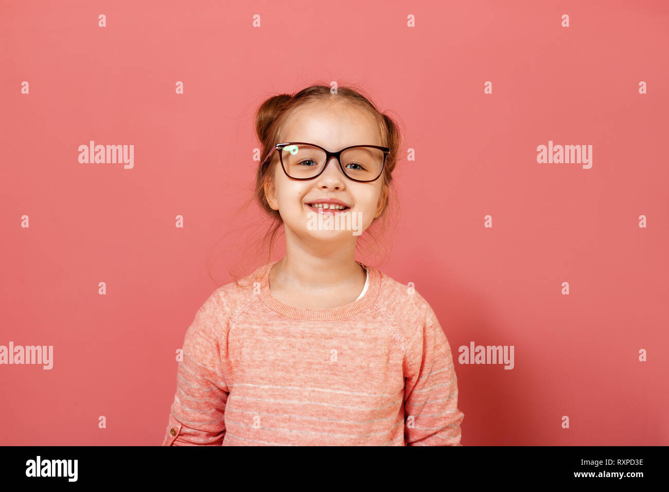 Ritratto di un grazioso piccolo 6 anno vecchia ragazza indossando occhiali su un sfondo rosa Foto Stock