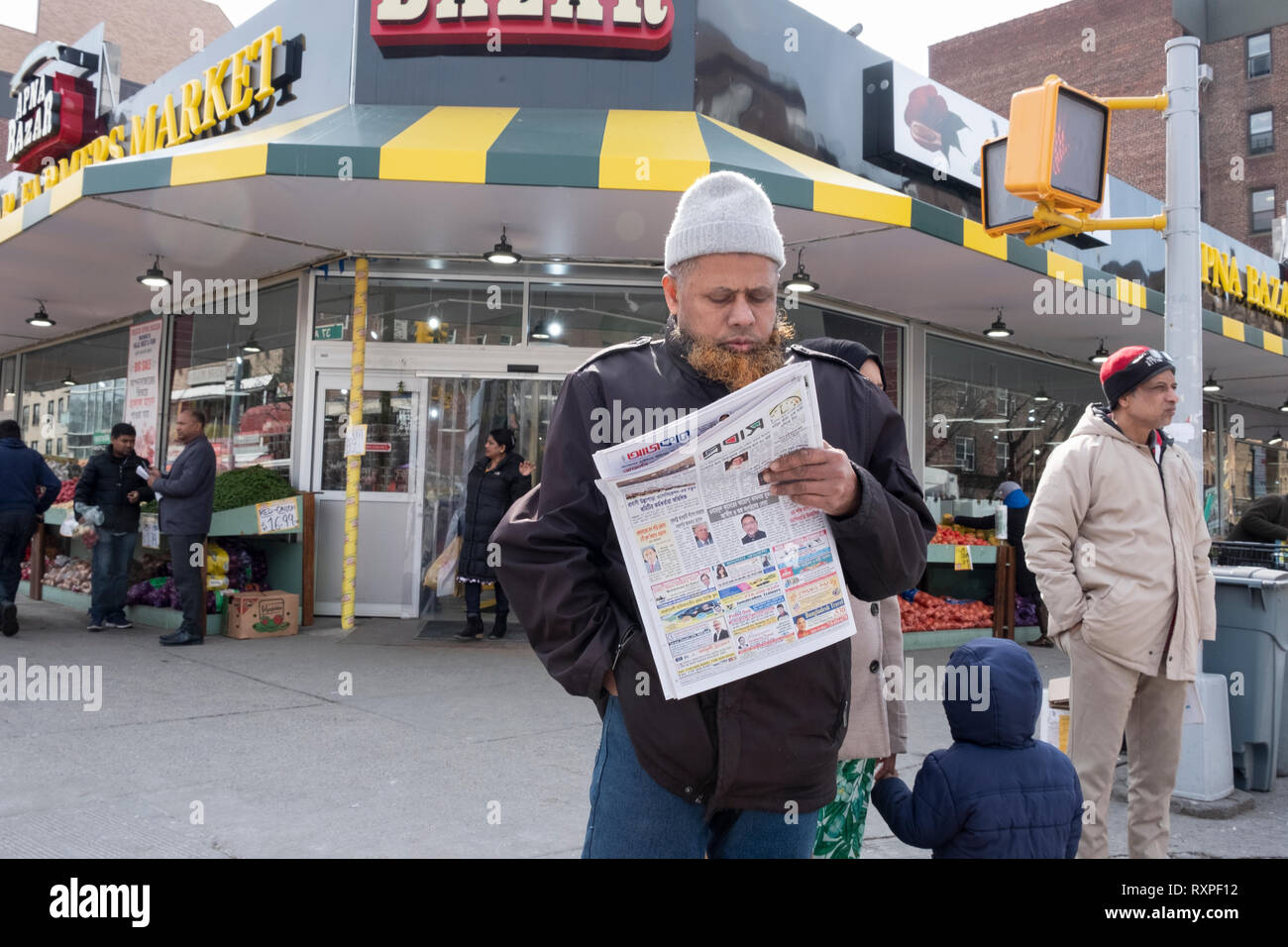 Un uomo musulmano con un henné barba tinto legge un giornale bengalesi sulla 37th Avenue a Jackson Heights, Queens, a New York City. Foto Stock