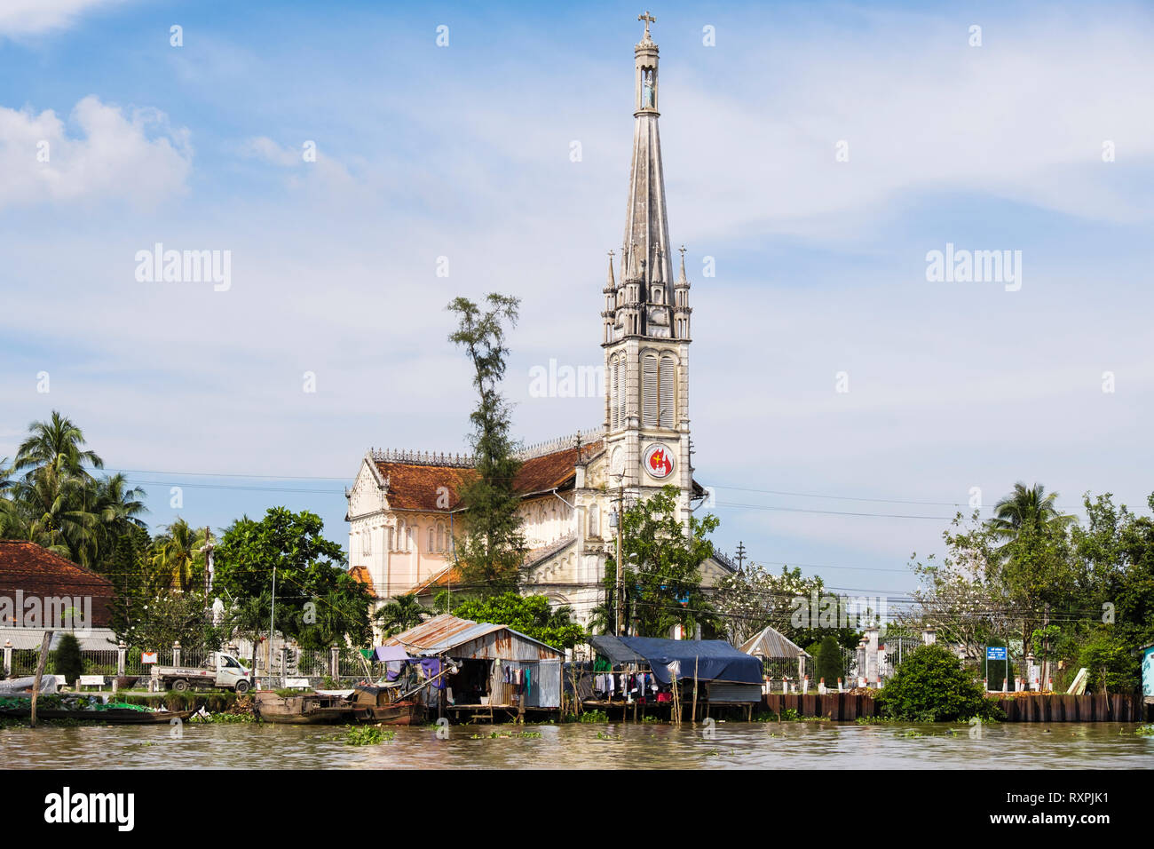 Xx secolo cattedrale cattolica Chiesa dietro tipica capanna di stagno palafitte sul lungofiume del Co Chien fiume nel Delta del Mekong. In Cai Be, Vietnam Foto Stock