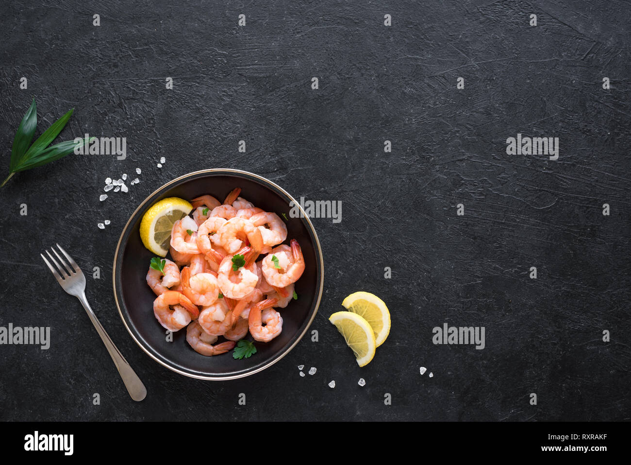 Gamberi, gamberetti nella ciotola, vista dall'alto, copia dello spazio. Piatti a base di frutti di mare freschi di sfondo - Code di gamberi su nero. Gamberi e bacchette. Foto Stock