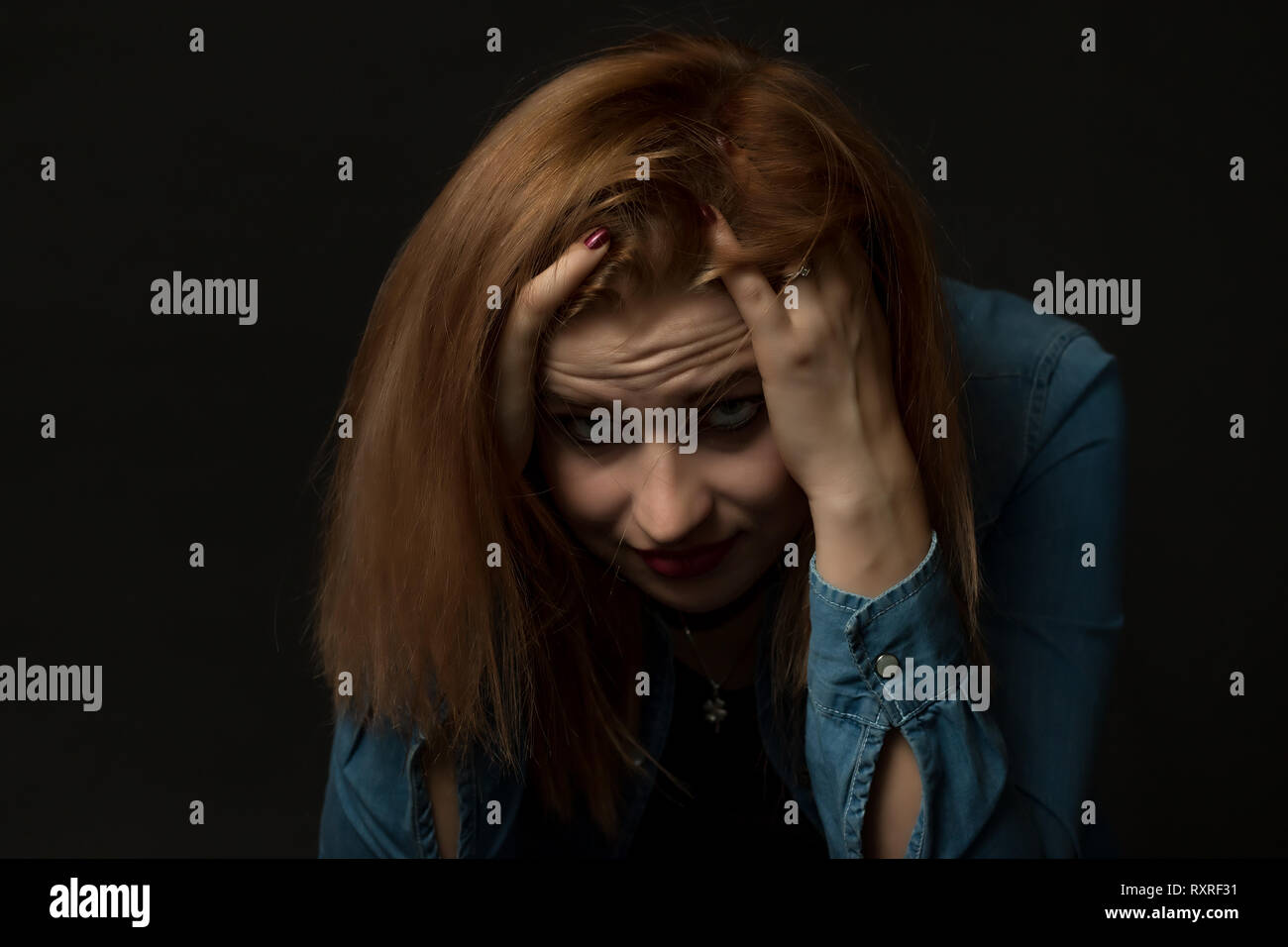 Tasto basso Ritratto di giovane donna in difficoltà la seduta e tenendo la testa con entrambe le mani e guardando la telecamera. Foto Stock