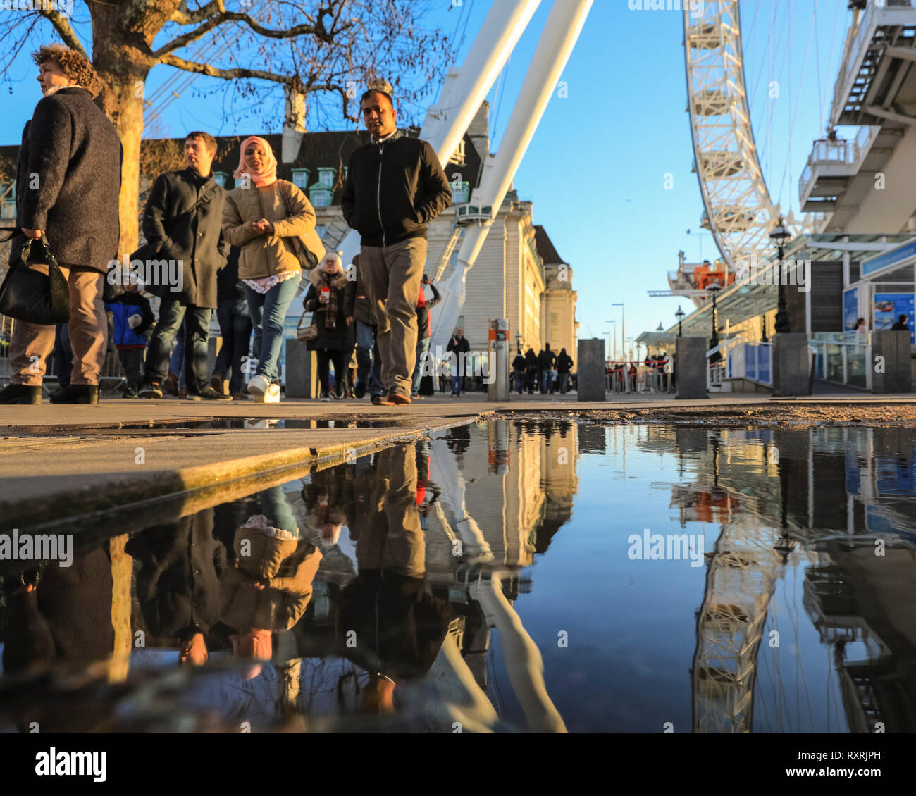 South Bank di Londra, Regno Unito. 10 mar 2019. La gente a piedi nel tardo pomeriggio di sole su Londra il South Bank. In seguito ad una giornata di sole e pioggia, il tardo pomeriggio vede un ritorno della serata calda luce solare con un sacco di pozzanghere e riflessioni vicino al London Eye. Credito: Imageplotter/Alamy Live News Foto Stock