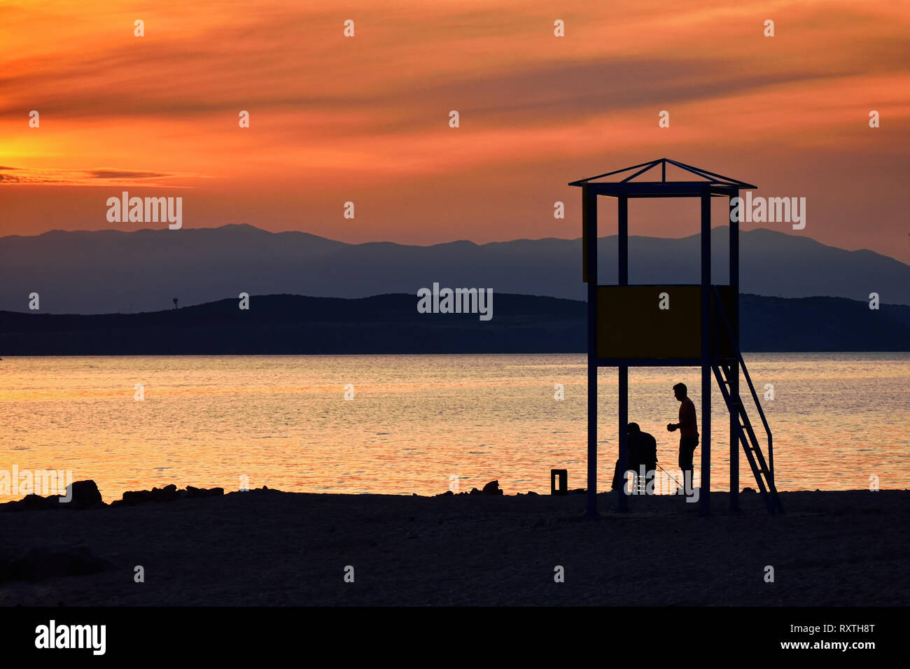 Sagome di due persone in riva al mare al tramonto, colori vibranti, la riflessione sulla superficie del mare Foto Stock