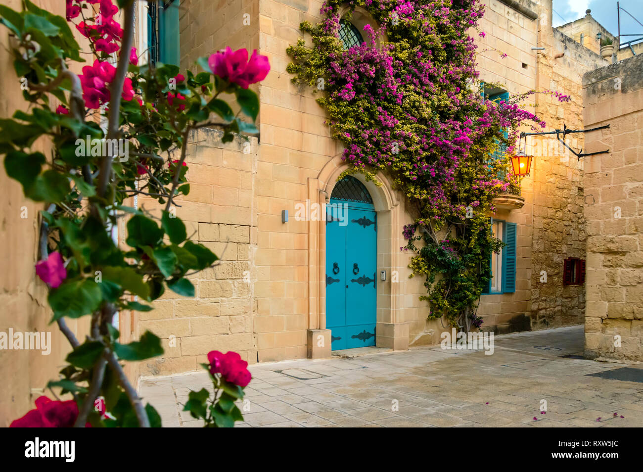 Mdina, Malta: tradizionale casa Maltese con artistiche porte, fiori di bouganville viola sulla parete di roccia calcarea e luci a lanterna Foto Stock